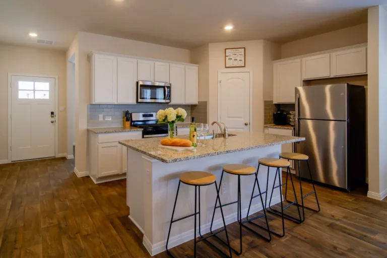 A modern kitchen with white cabinets, a central island with stools, and stainless steel appliances.